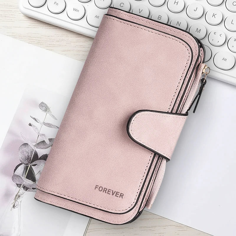 A pink leather zipper wallet with a rounded edge and the word forever embossed on it, placed next to a white laptop keyboard.