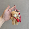 A fluffy brown teddy bear plush toy attached to a red keychain with a camera and glasses.