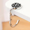 A silver zinc alloy folding handbag hook with a black and white spotted leather charm resting on a white surface.