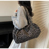 A person is holding a leopard print canvas tote bag with an adjustable shoulder strap against a light-colored vertical blind.