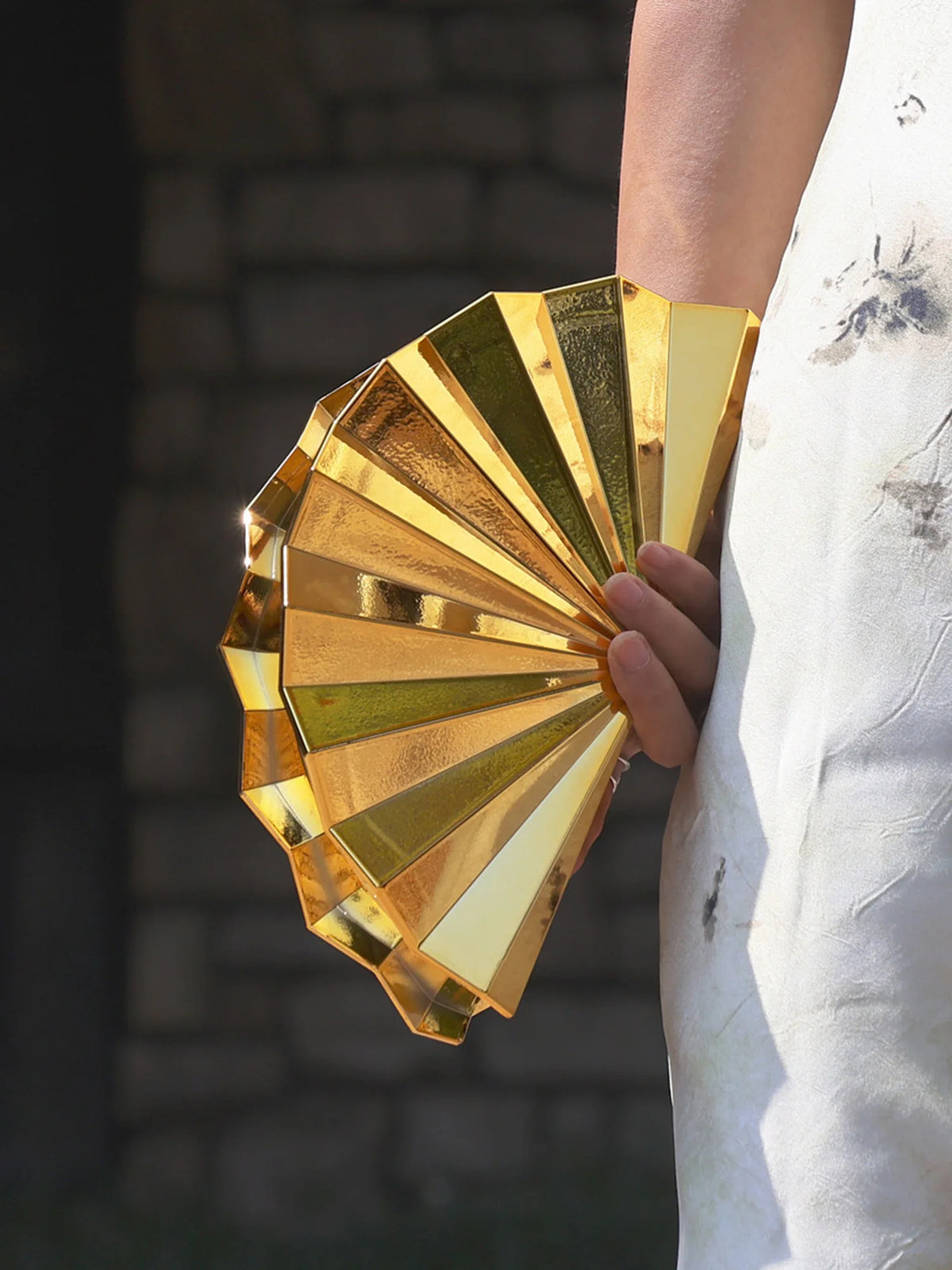 A hand holds a gold acrylic chain crossbody bag, displaying its layered, reflective surface.