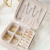 A light pink compact leather jewelry travel box with velvet lining displaying silver and gold rings and necklaces.