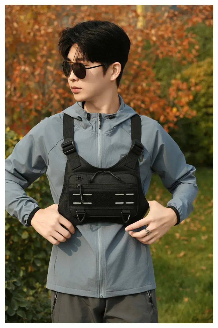 A young man wearing a gray tactical chest rig vest bag while standing outdoors.
