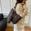 A woman holds a brown geometric tote bag with leather trim against a white background.