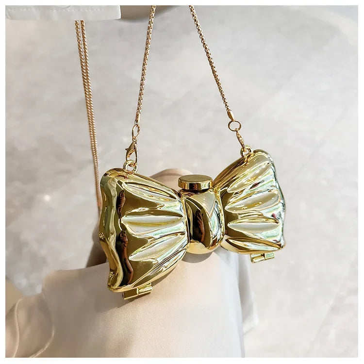 Gold heart-shaped acrylic evening clutch with a delicate chain strap being held by a hand.