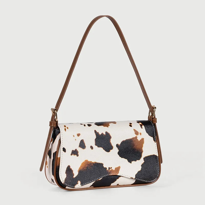 A brown leather single shoulder bag featuring a cow print pattern with black and white spots.