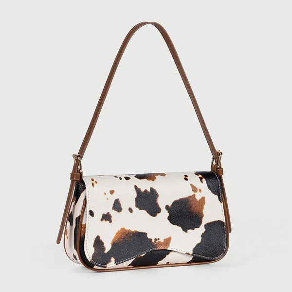 A brown leather single shoulder bag featuring a cow print pattern with black and white spots.