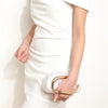 A woman wearing a white dress holds an elegant gold-tone evening clutch bag.