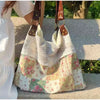 A white and floral patchwork shoulder bag with a mesh top and brown leather straps is displayed outdoors.