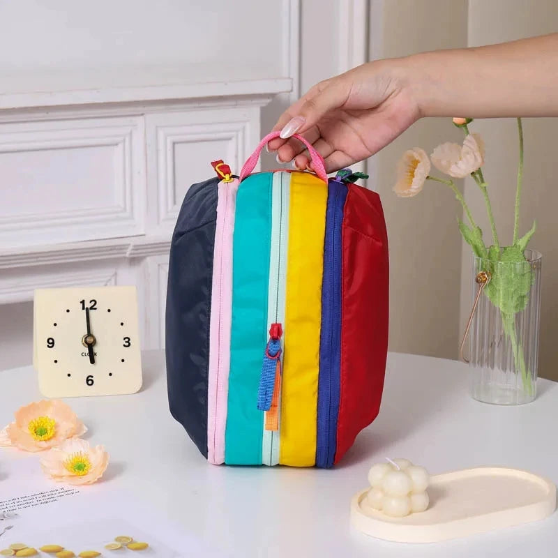 A vertical travel makeup bag featuring bright dopamine colors like blue, green, yellow, and red, resting on a white surface.