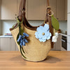 A tan woven leather shoulder bag with brown straps and blue and white floral charms