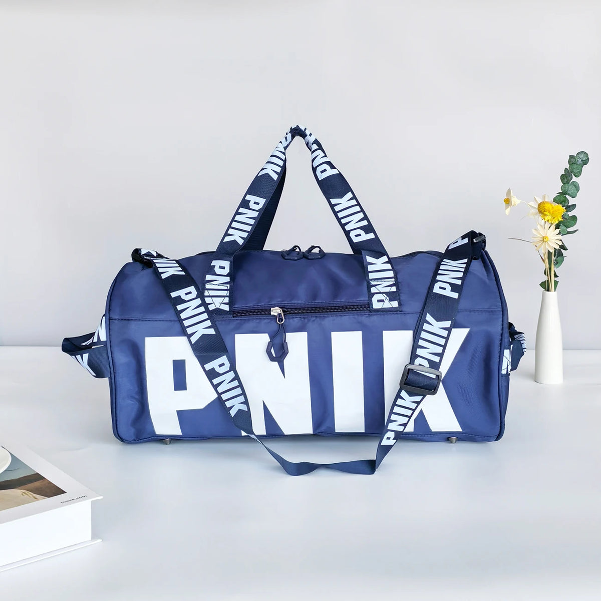 A navy blue shoulder bag with white lettering and striped straps is displayed on a white surface.