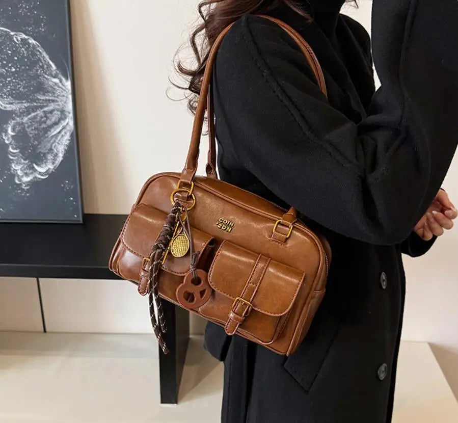 A brown leather vintage letter print crossbody bag carried by a person wearing a black coat.