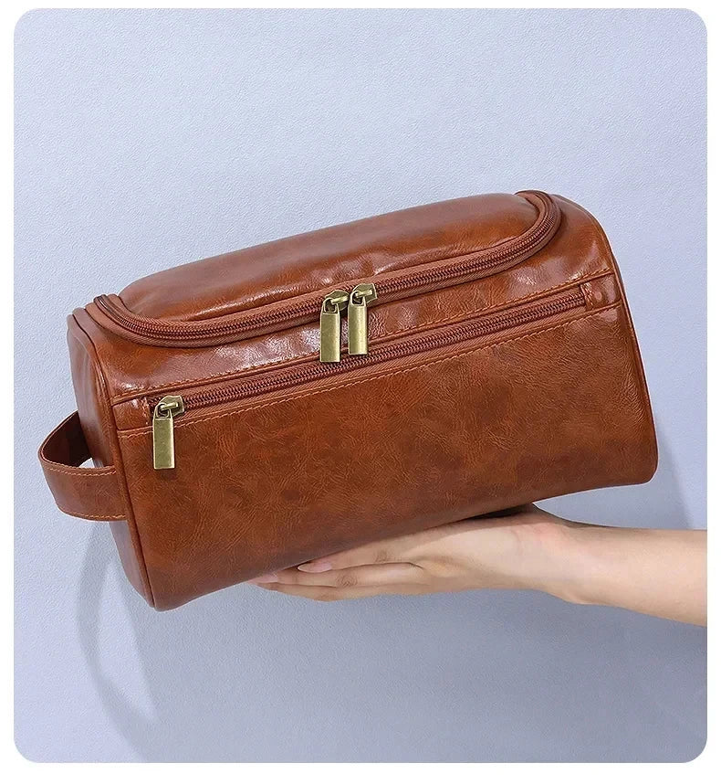 A brown leather toiletry bag with a zipper closure is held in a person's hand.
