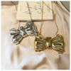A gold-toned bow knot evening bag with a silver bow detail is displayed against a light beige fabric next to a book.