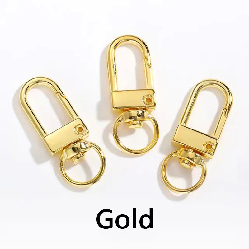 Drei goldfarbene, drehbare Karabinerhaken für Taschen und Gürtel vor weißem Hintergrund.