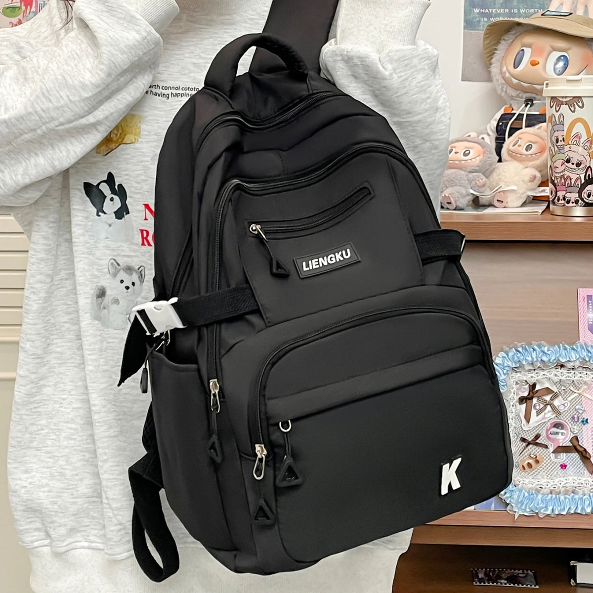 A black lightweight nylon college backpack is shown being held by a person, with other items visible in the background.