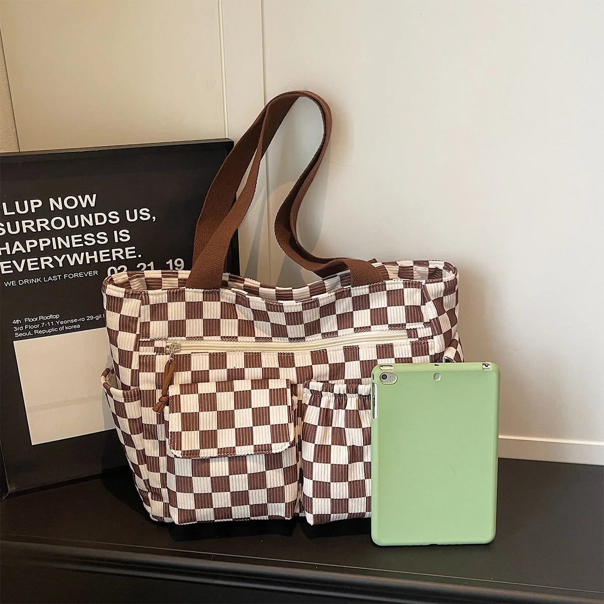 A brown and beige stripe pattern corduroy tote bag with leather handles resting on a dark surface.