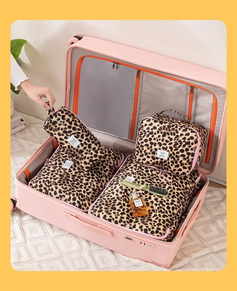 A pink travel makeup organizer bag with an open lid displaying leopard print cosmetic pouches and a brush.