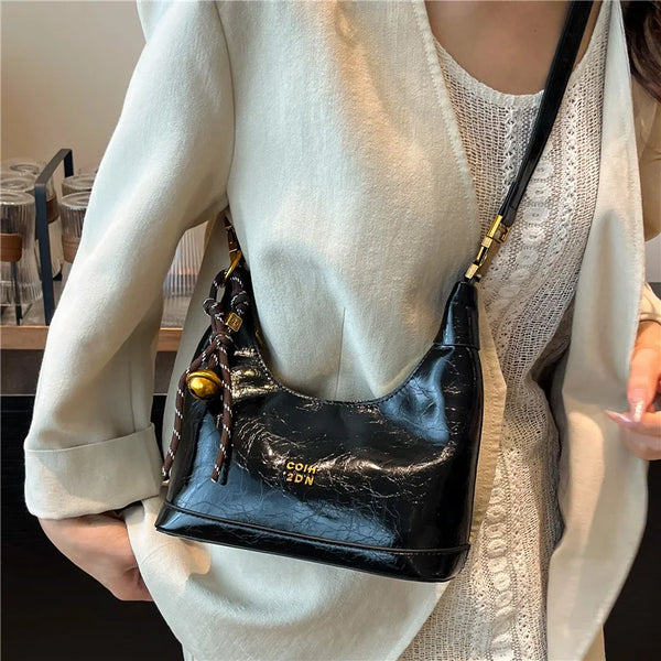 Schwarze Retro-Leder-Schultertasche mit goldenen Verzierungen, getragen von einer Person in einem hellbeigen Blazer.