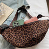 A close-up of a brown leopard print crossbody bag with a pink interior lining and a dark leather strap, resting on a denim sh