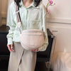 A light mint green shirt model holds a pale pink soft leather crossbody bag with a strap.