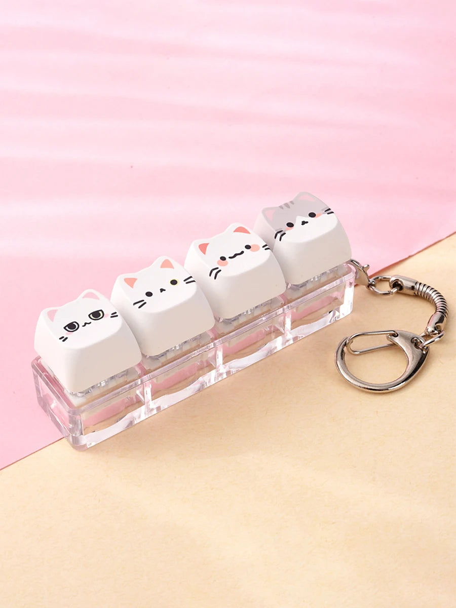 A clear plastic case holding several white kawaii cat keycaps and a silver keyring.