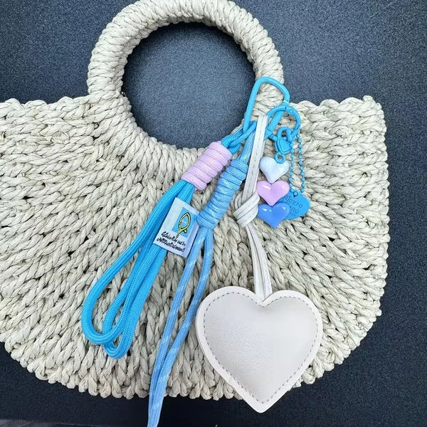 Handmade PU leather heart keychain with braided rope on a light beige woven bag.