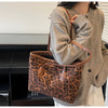 A woman holds a brown leopard print vintage tote bag against a light gray knitted sweater.