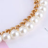 A close-up of an elegant gold chain shoulder strap featuring multiple round white pearls.