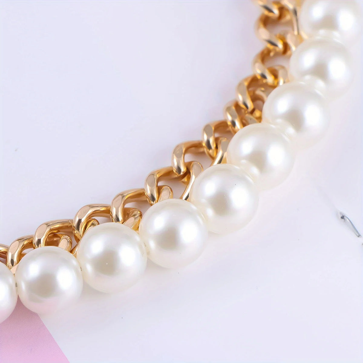 A close-up of an elegant gold chain shoulder strap featuring multiple round white pearls.