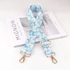 Blue floral patterned diagonal shoulder strap for bags displayed next to a product box.