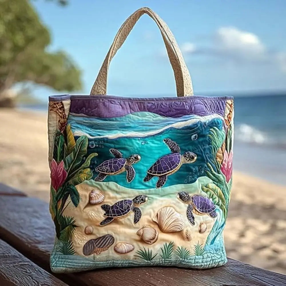 A purple and green quilted canvas tote bag featuring various sea turtles and seashells on a sandy beach background.