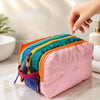 A pink multi-compartment toiletry organizer bag with colorful accents is held by a hand on a marble surface.