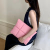 A woman is holding a pink quilted laptop sleeve in a dark denim dress.