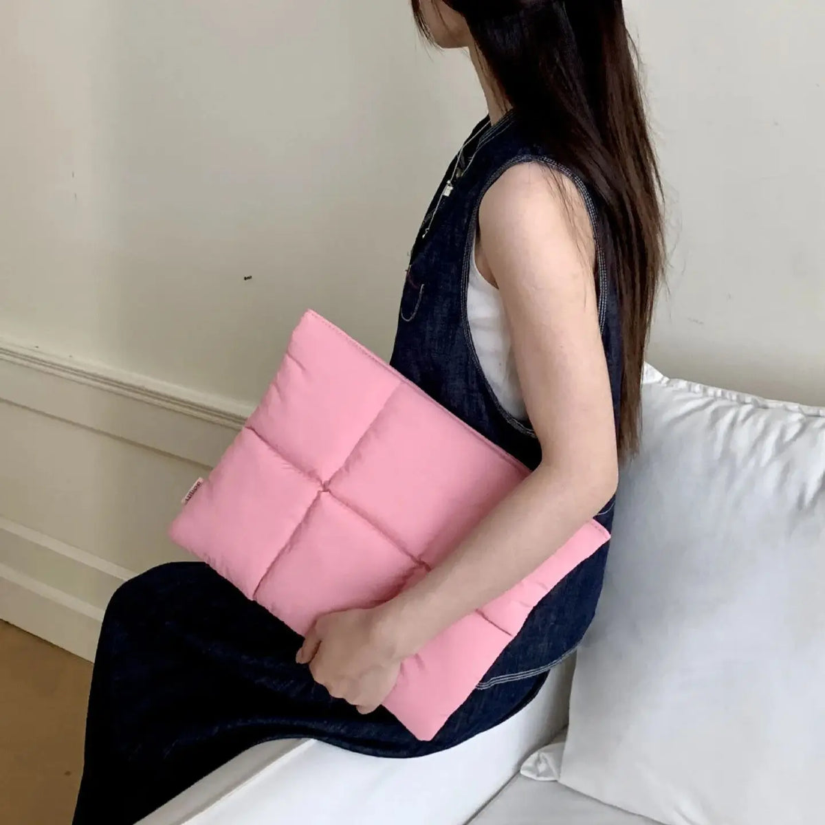 A woman is holding a pink quilted laptop sleeve in a dark denim dress.