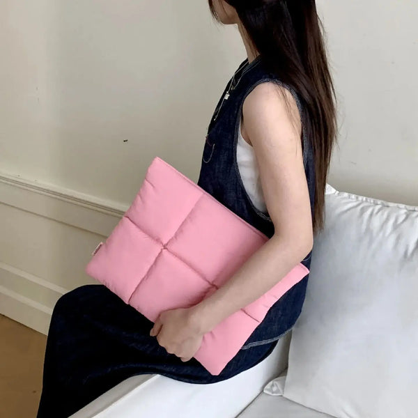 A woman is holding a pink quilted laptop sleeve in a dark denim dress.