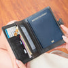 A hand holds an open black leather passport wallet displaying a British passport and other cards.