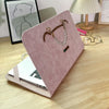 A pink slim PU laptop protective case with a leather strap and a silver chain charm resting on a wooden table.