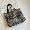 A floral patterned bohemian corduroy tote bag resting on a white fabric and next to a white garment.