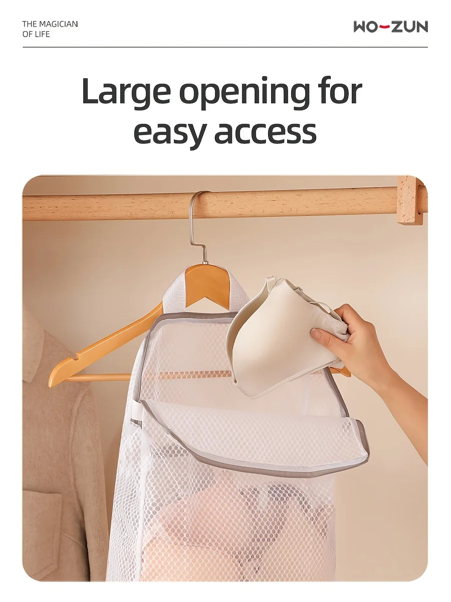 A hand is hanging a white honeycomb mesh laundry bag onto a wooden wall-mount hook.