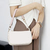 A woman holds a cream-colored leather shoulder bag with a pink strap against a white background.