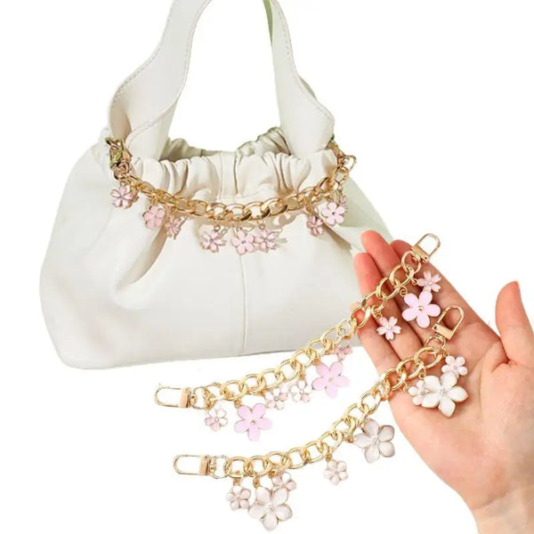 A white bag with a gold chain accessory featuring enamel hearts and cherry blossoms