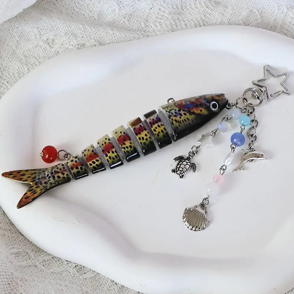 A simulation fish keychain featuring colorful scales and a silver charm on a white plate.