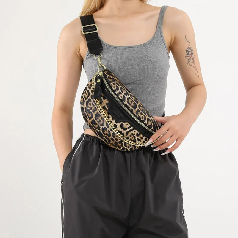 Eine Frau hält eine Leopardenmuster-Umhängetasche mit schwarzem Riemen und goldfarbenem Hardware.