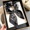 Black paisley silk hair scarf tied in a bow displayed in a wooden frame.