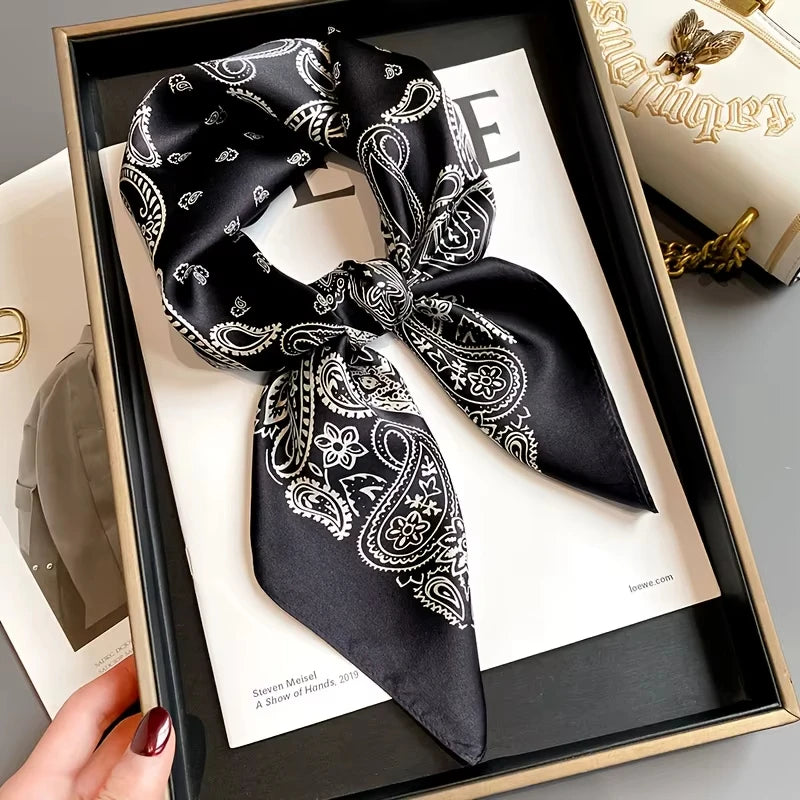 Black paisley silk hair scarf tied in a bow displayed in a wooden frame.