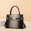 A black crocodile print shoulder handbag with a brown leather handle and gold hardware.