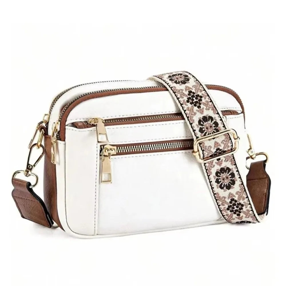 A white leather crossbody bag with a brown patterned strap and gold hardware.