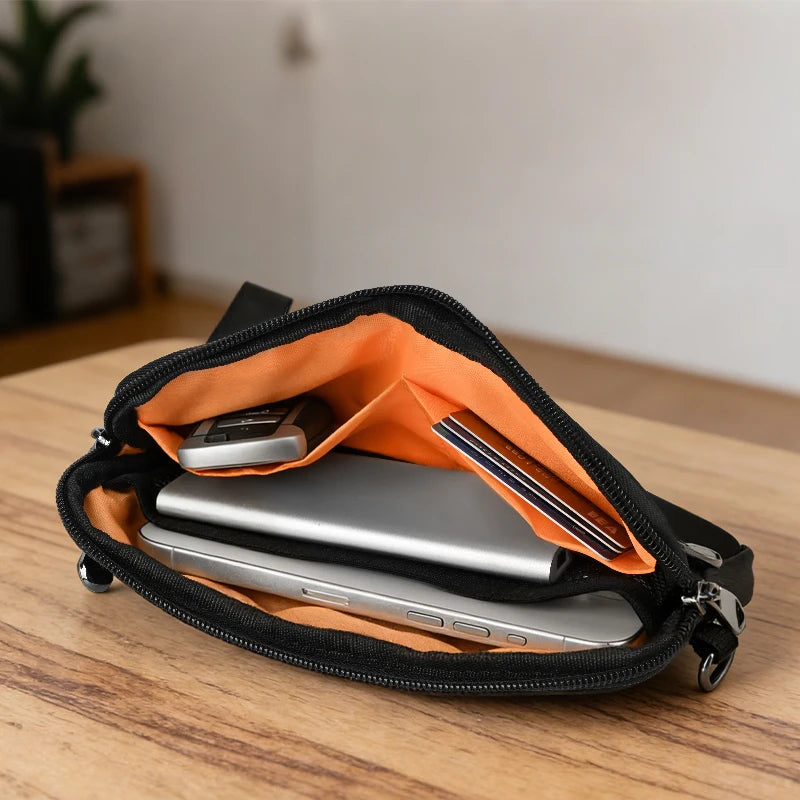 A black zippered phone pouch with an orange lining and a wrist strap, holding a silver laptop.